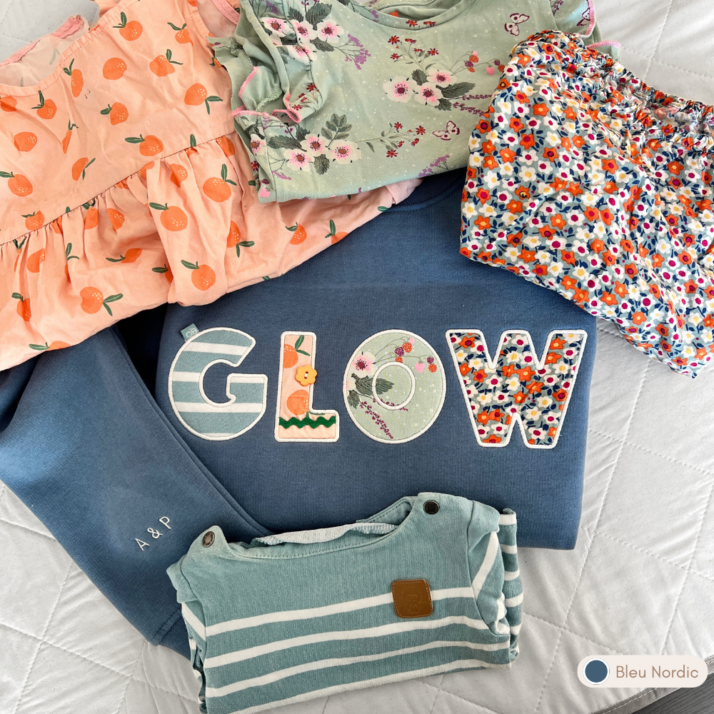 Sweat personnalisé femme col rond bleu nordic brodé « GLOW », appliqués fleuris colorés, initiales brodées sur la manche