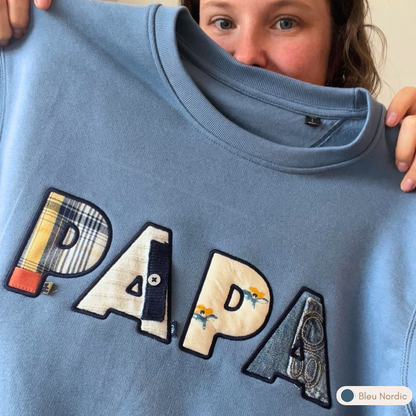 Sweat souvenir personnalisé homme col rond bleu nordic brodé « PAPA », appliqués tissus vêtements de bébé recyclés, porté par un papa